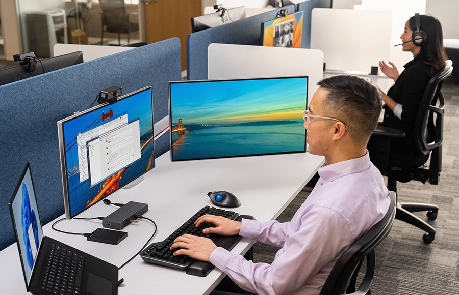 A man in a video call, while a woman utilises a docking station to connect multiple devices.