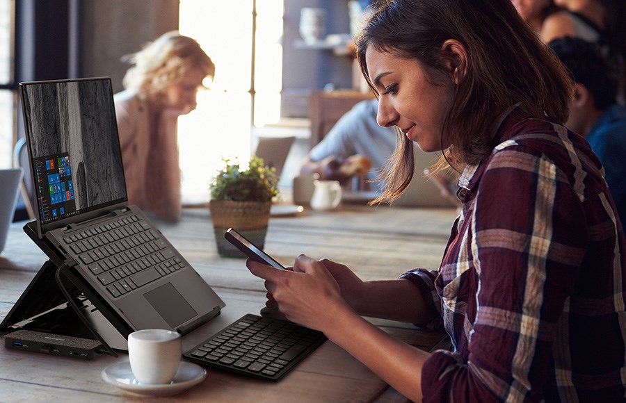 una mujer en un café usando su docking station portátil para conectar su notebook con facilidad.