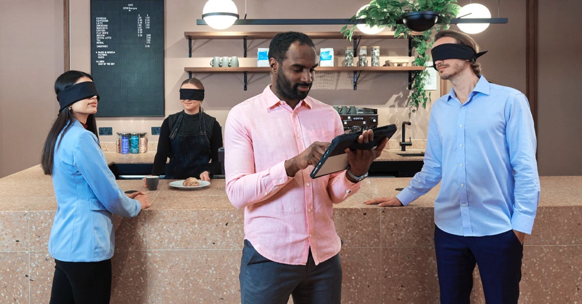 Person looking at tablet with people in the background wearing blindfolds