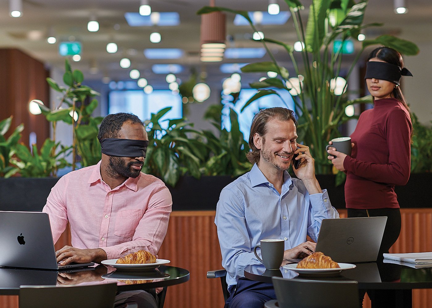 Two persons glance mischievously at a man's screen. He uses a privacy screen to safeguard his onscreen data.