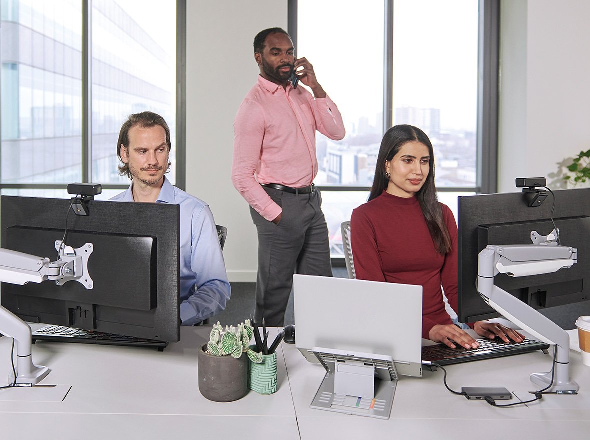 Two men glance mischievously at a woman's screen. She uses a privacy screen to safeguard her onscreen data.