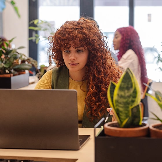 Woman sitting in office with plant and laptop on desk using a Kensington EQ Privacy Screen Filter. 