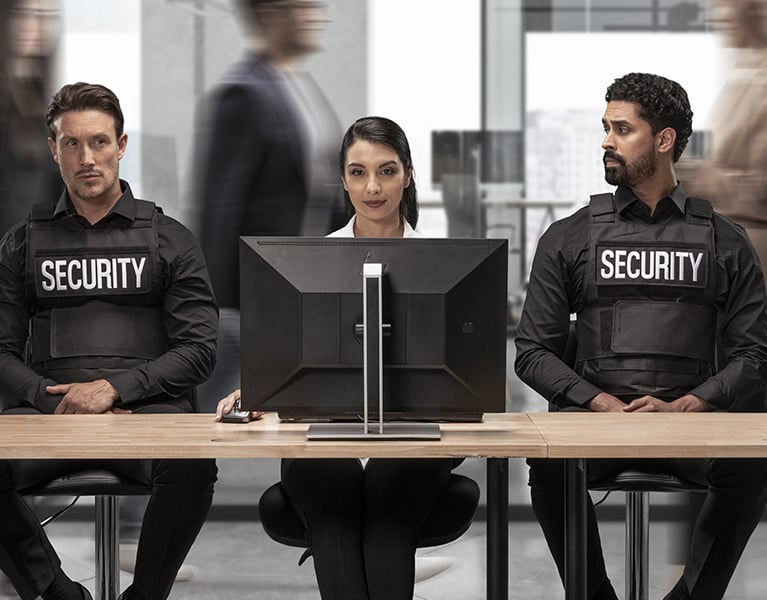 Woman in office at desktop with two security guards sitting next to her.