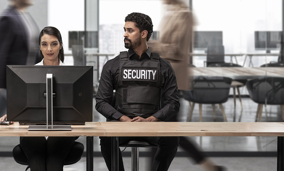 Woman in office at desktop with two security guards sitting next to her.