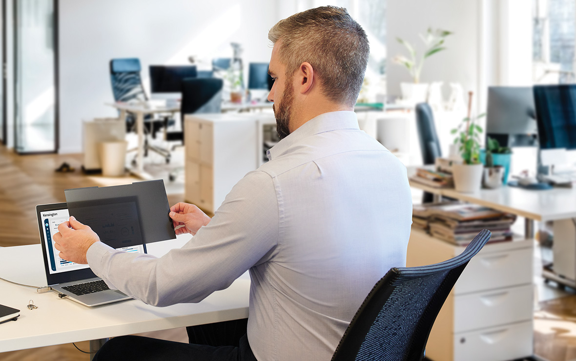 Man at desk putting a Kensington privacy screen on laptop.