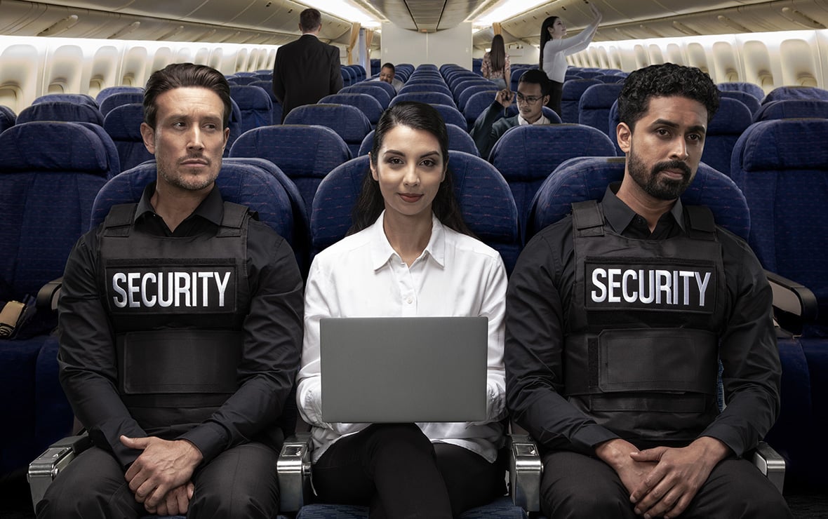 Woman on plane sitting between two security guards using laptop with Kensington privacy screen with limited side viewing. 