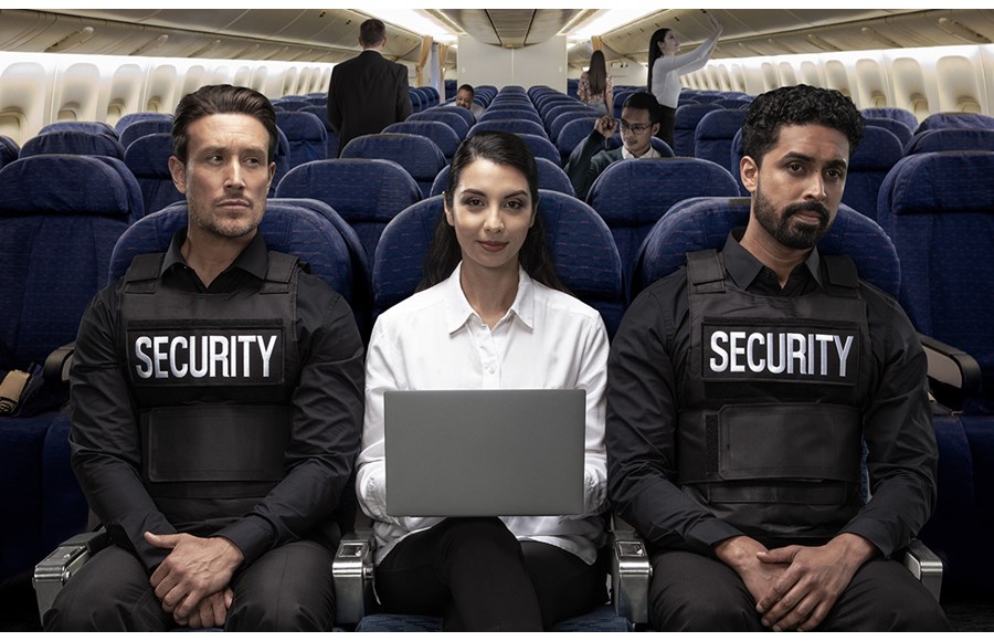 Woman on plane sitting in between two security guards using laptop with Kensington privacy screen with limited side viewing.