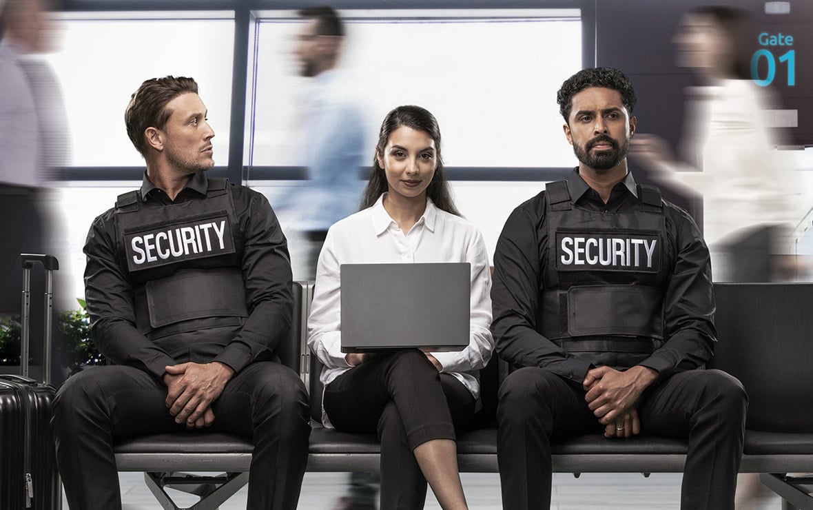 Woman on bench sitting between two security guards using her laptop with a Kensington privacy screen. 